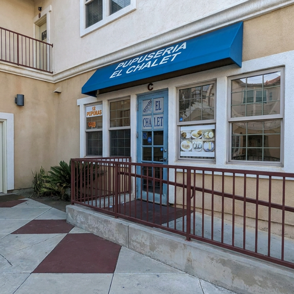 Exterior entrance of Pupuseria El Chalet, featuring a blue awning, accessible ramp, and food photos displayed in the windows.