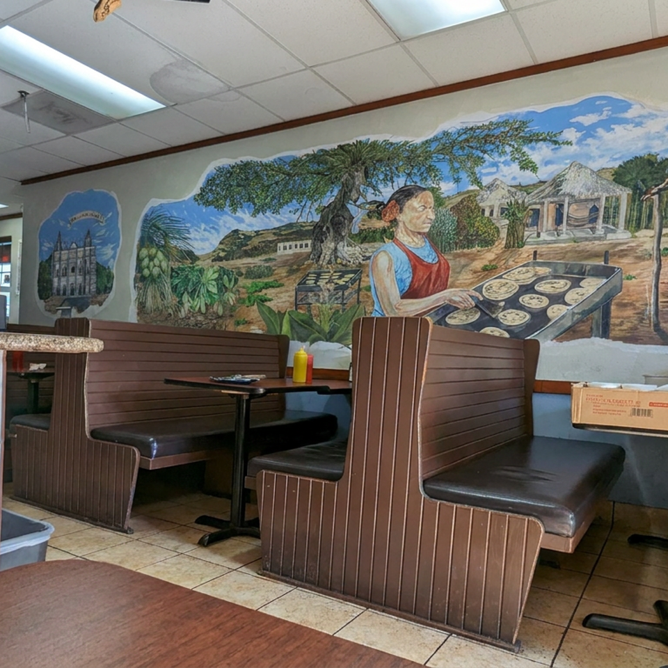 Cozy restaurant dining area with brown booths, tables, tiled floors, and a colorful mural depicting a woman serving pastries.
